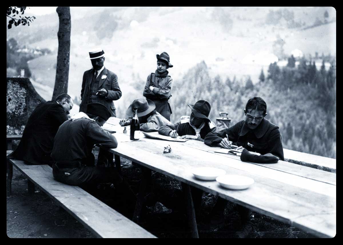 Boys scouts écrivant dans les environs de Grenoble, en 1913, assis autour d'une table - Source : Gallica.bnf.fr